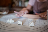 From above of crop anonymous woman in apron rolling dough on table while preparing dumplings with meat in kitchen