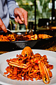 A chef carefully garnishes a flavorful lobster pasta dish with fresh herbs, served on a white plate in an elegant setting