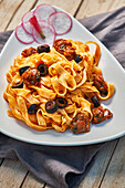 A delicious serving of fettuccine pasta with black olives, sun-dried tomatoes, and a rich tomato sauce, presented on a white plate