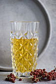 Ein mit goldenem Apfelwein gefülltes Kristallglas, begleitet von getrockneten roten Beeren vor einem strukturierten grauen Hintergrund