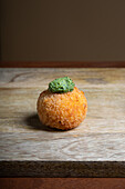 A crispy rice and cheese arancini garnished with basil pesto, presented on a rustic wooden table.