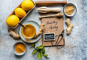 Eine flache Komposition mit Zitronen, Ingwer, Honig und Gewürzen neben einem Notizblock mit der Aufschrift "Gesunde Ernährung", die das Thema Wellness und natürliche Lebensmittel aufgreift