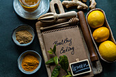 A flat lay of healthy food ingredients with a notebook labeled 'Healthy Eating', surrounded by spices, lemon, and tea