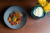 From above sophisticated plate of grilled vegetable stew with yellow pepper, onion, and a crisp sourdough cracker.
