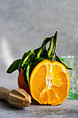 A vibrant, fresh cut orange with green leaves beside a wooden juicer on a neutral background