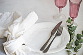An elegant table setting featuring white embossed plates, vintage silverware, and pink glassware, accented with a sprig of eucalyptus
