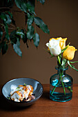 Elegante Präsentation von gegrilltem Hähnchen auf Bohnen, garniert mit Kräutern, auf einem dunklen Teller, ergänzt durch eine Glasvase mit gelben Rosen.