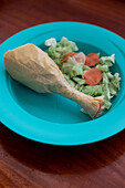 A fake chicken drumstick made from a twisted plastic bag accompanied by paper cutout salad on a bright blue child's plate.