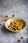 Bowl of salty coated peanuts on a textured surface with some scattered around the bowl
