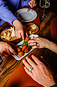 Eine Gruppe von Freunden greift nach köstlichen Tapas auf einem Teller bei einem warmen und freundlichen Abendessen, teilt das Essen und genießt die Gesellschaft des anderen