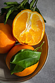 Oranges with vibrant green leaves placed in a bowl, highlighted by natural sunlight
