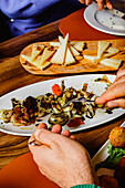 A person serving gourmet pasta from a shared plate, with a cheese platter in the background, in a warm, intimate dining setting