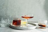 Eine Auswahl an alkoholischen Getränken in strukturierten Gläsern, die elegant auf einem runden Betontablett vor einem weichen grauen Hintergrund präsentiert werden