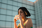 A stylish woman sips water from a glass bottle against the modern backdrop of Madrid's Four Towers Business Area.