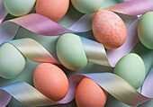 Draufsicht auf pastellfarbene Ostereier, die zwischen seidigen Bändern eingebettet sind, eine einladende Feier des Osterfestes.