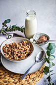 A nutritious granola breakfast served in a white bowl, accompanied by a glass bottle of milk and eucalyptus sprigs for a fresh look