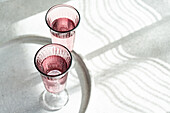 Von oben werfen drei rosa Gläser in einer Reihe komplizierte Schatten auf eine weiße, strukturierte Oberfläche, wodurch ein abstraktes Muster entsteht. Generatives AI-Bild