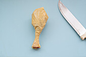 An artful display of a chicken drumstick made from a plastic bag, presented on a ceramic plate with a knife beside it, symbolizing food contamination by plastic waste.
