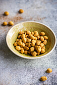 Bowl of salty coated peanuts on a textured surface with some scattered around the bowl
