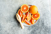 From above plate with segments of ripe oranges and a whole orange beside a wooden citrus juicer on a textured background.
