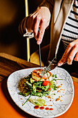 Person using tongs to serve sophisticated grilled dish with fresh salad on a marbled plate