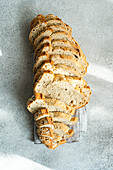 Top view of long loaf of seeded sourdough bread, sliced and arranged in a row on a linen cloth with a textured gray background