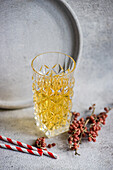 Elegantly textured glass filled with cider beside red berries and a striped straw on a concrete backdrop