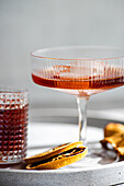 A close-up view of sophisticated alcoholic beverages, featuring a stemmed glass with rosy-hued liquor and a textured glass filled with cherry liqueur over ice