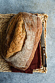 From above of crusty loaf of homemade rye sourdough bread placed on a woven mat with a dark red napkin and a bread knife