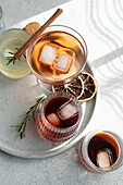 From above of assorted alcoholic drinks in textured glasses, garnished with cinnamon, rosemary, and dried citrus, on a round tray
