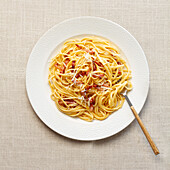 Eine Draufsicht auf eine traditionelle italienische Spaghetti Carbonara auf einem weißen Teller, garniert mit geriebenem Käse und gepökelten Fleischstückchen.