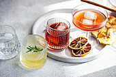 Eine Sammlung verschiedener Spirituosen in gerippten Gläsern, darunter Kirschlikör mit Eis, Limoncello mit einem Rosmarinzweig und andere, die alle auf einem Tablett mit getrockneten Zitrusfrüchten stehen