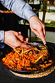 A person serves a sumptuous seafood pasta dish from a large pan at an al fresco dining event