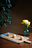 Gourmet baby potato canapé topped with melted mozzarella cheese and grilled red pepper, artistically presented on a wooden board with a vibrant yellow rose in the background.