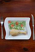 From above conceptual image of a plate with food items crafted from plastic bags, alongside real cutlery, on a wooden table.