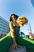 A cheerful woman in a green jumpsuit offers a juicy burger in front of the iconic Cuatro Torres business area of Madrid, Spain, showcasing a vibrant urban lifestyle.