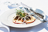 Herb herring fillet on apple slices with onion rings