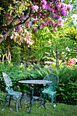 Romantische Gartenecke mit gusseisernen Möbeln unter blühendem Rhododendron