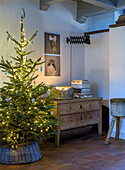 Illuminated Christmas tree next to rustic chest of drawers and wall pictures