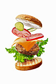 Burger with flying ingredients: Bun, lettuce, tomato, cheese, meat and cucumber