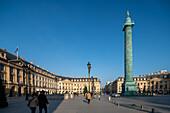 Pedestrians walking near the Vendome Column under a clear blue sky.