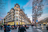 Menschenmengen schlendern bei Zara an der Ecke Champs-Élysées und Berri, während der Abend in Paris hereinbricht.