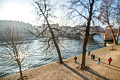 Fußgänger, die an einem sonnigen Wintertag am Ufer der Seine spazieren gehen, mit Weichzeichner aufgrund eines Tilt-Shift-Objektivs.