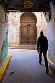 Ein junger Mann geht durch eine enge Gasse in den labyrinthartigen Straßen der Medina von Fez, Marokko.