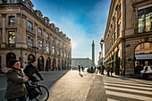 Sonnenlicht beleuchtet die Rue de la Paix, während Fußgänger die Place Vendôme in der Ferne sehen.