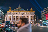 Das Opernhaus Palais Garnier in der Abenddämmerung mit dem geschäftigen Treiben der Stadt im Vordergrund.