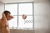 Mann unter der Dusche schaut in den Spiegel