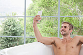 Lächelnder Mann in der Badewanne, der ein Selfie macht