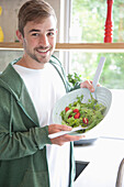 Mann hält lächelnd eine Schüssel mit Salat