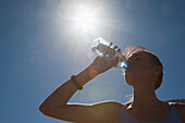 Frau trinkt Wasser aus einer Flasche gegen den blauen Himmel